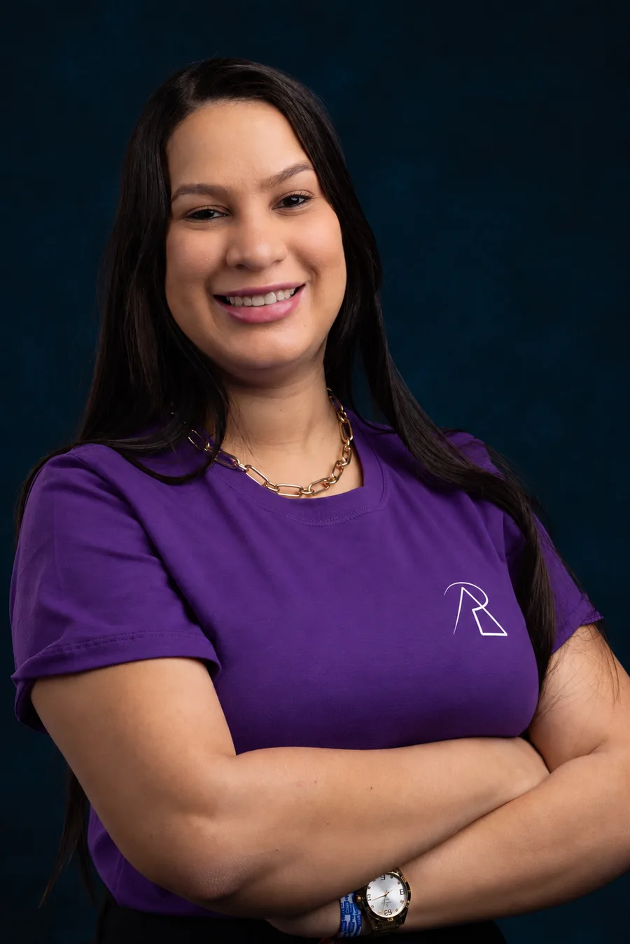 Aline Prado, de camiseta roxa, braços cruzados e sorrindo